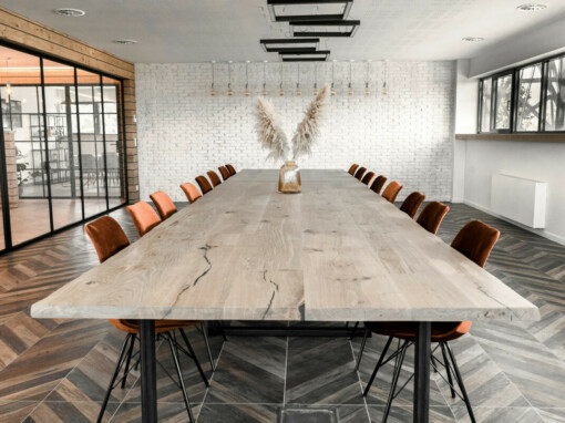 Salle de réunion moderne avec du parquet au sol et une table en bois avec un vase et des fleurs séchées.