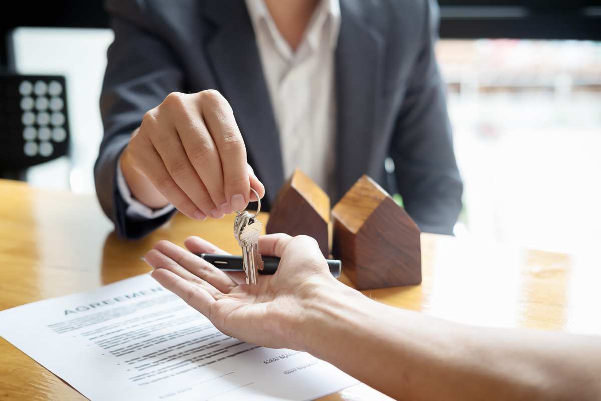 Agent immobilier tendant les clés d'une maison qu'il vient de vendre vers une main ouverte