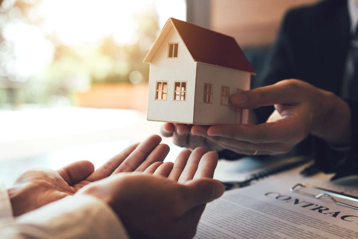 Mains d'un agent immobilier tendant vers les mains d'un acheteur une petite maison en papier